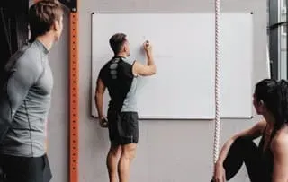 A fitness business owner leading a whiteboard strategy session in a modern gym environment, discussing growth planning with a team.